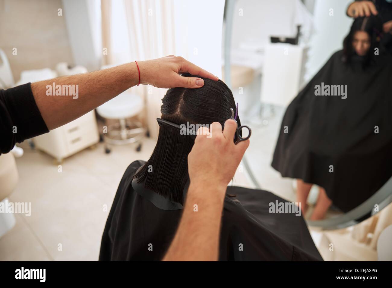 Coiffeur professionnel avec un peigne travaillant sur sa coiffure de client Banque D'Images
