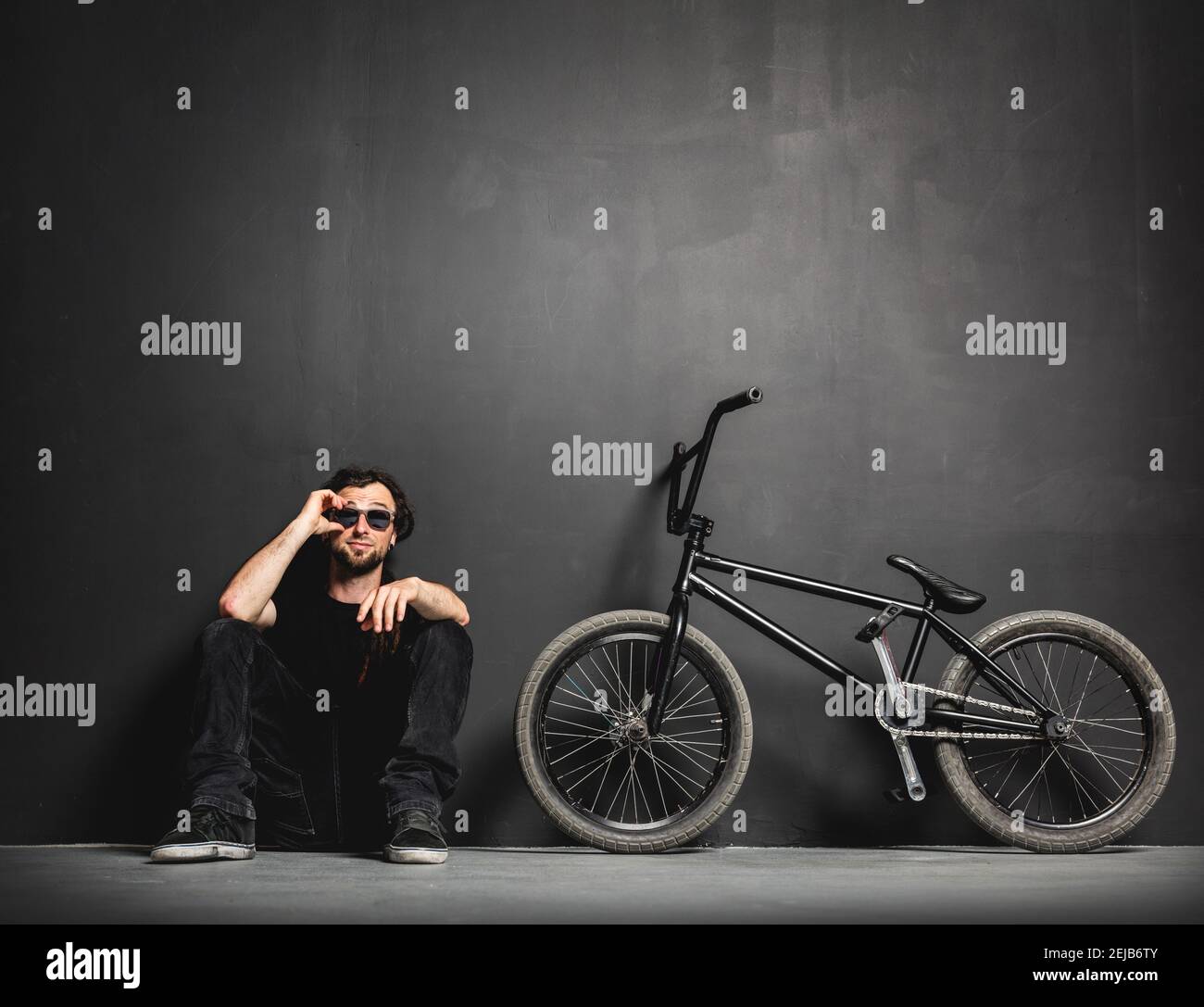 Homme assis à côté de son vélo BMX, en ajustant ses lunettes de soleil. Un  lieu de détente décontracté. Détente Photo Stock - Alamy