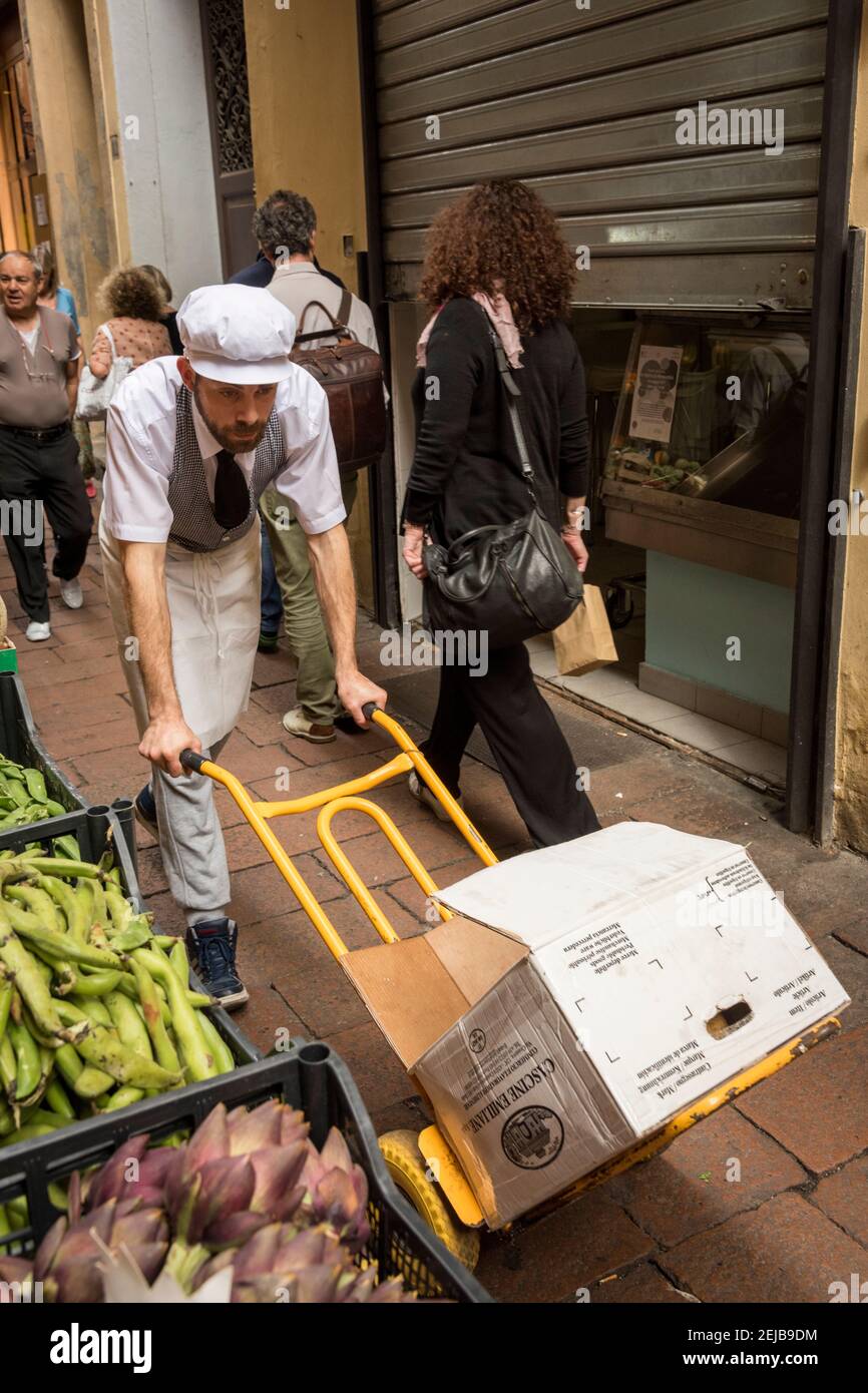 Un homme poussant un sac de chariot dans une rue étroite après les boutiques de fruits et légumes dans la zone de marché de bologne Italie Banque D'Images