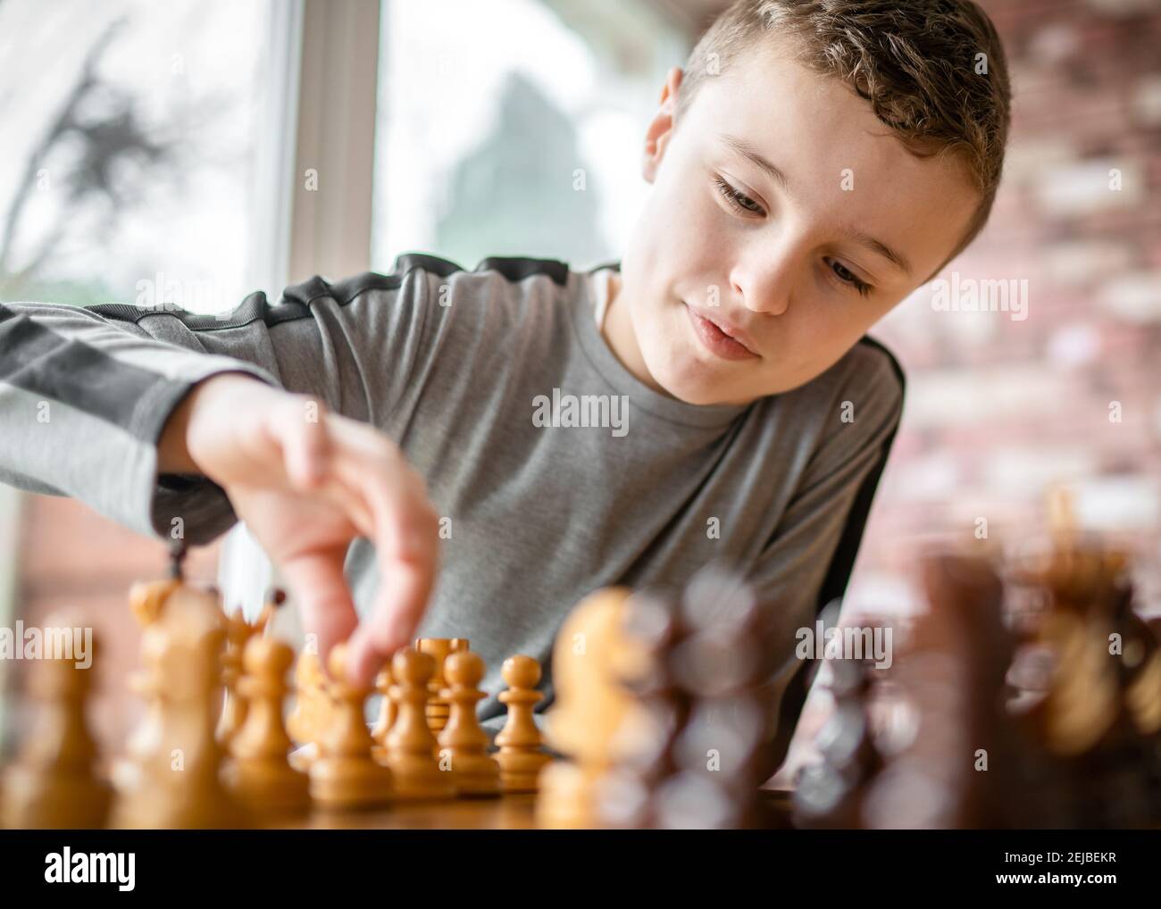 Mignon jeune heureux garçon génie d'échecs se concentrant jouant à la partie de stratégie pièce mobile assise à une table en bois avec échiquier été ensoleillé Banque D'Images