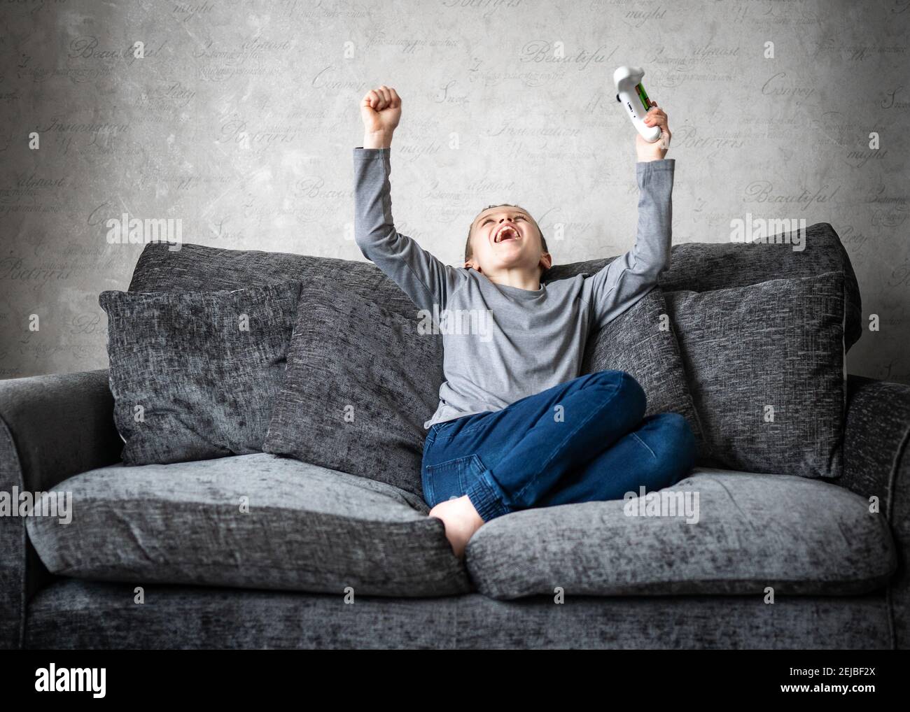 Jeune adorable petit garçon assis sur un canapé avec ordinateur manette de jeu de console de manette de bras dans l'air acclamations criant avec excitation après avoir gagné le jeu Banque D'Images