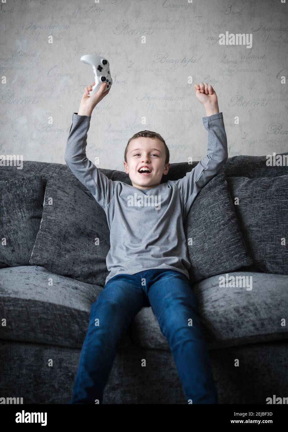 Jeune adorable petit garçon assis sur un canapé avec ordinateur manette de jeu de console de manette de bras dans l'air acclamations criant avec excitation après avoir gagné le jeu Banque D'Images