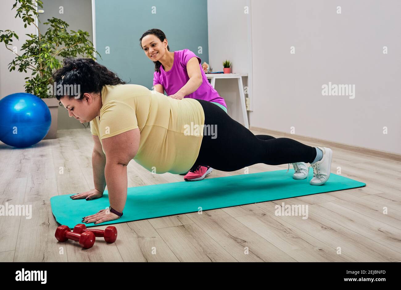 Une femme en surpoids fait des exercices avec un entraîneur personnel. Brunette plus-size faisant des push-up sur un tapis de fitness Banque D'Images