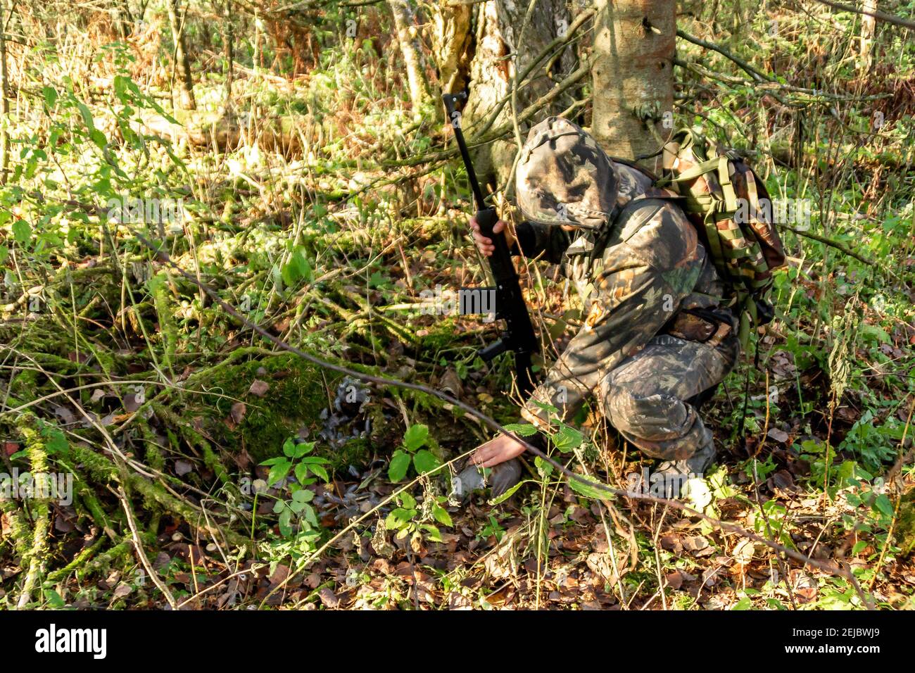 le tétras de grenaille est tombé sous des branches couvertes de mousse, les plumes éparses se trouvent autour, le chasseur avec l'arme enroulée près de la proie Banque D'Images