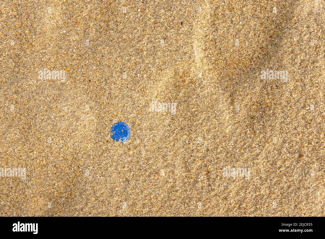 Bouchon de bouteille d'eau bleu dans le sable de plage, concept de pollution plastique Banque D'Images