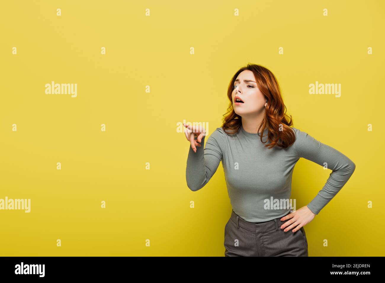femme avec les cheveux bouclés debout avec la main sur la hanche pendant en pointant avec le doigt sur le jaune Banque D'Images