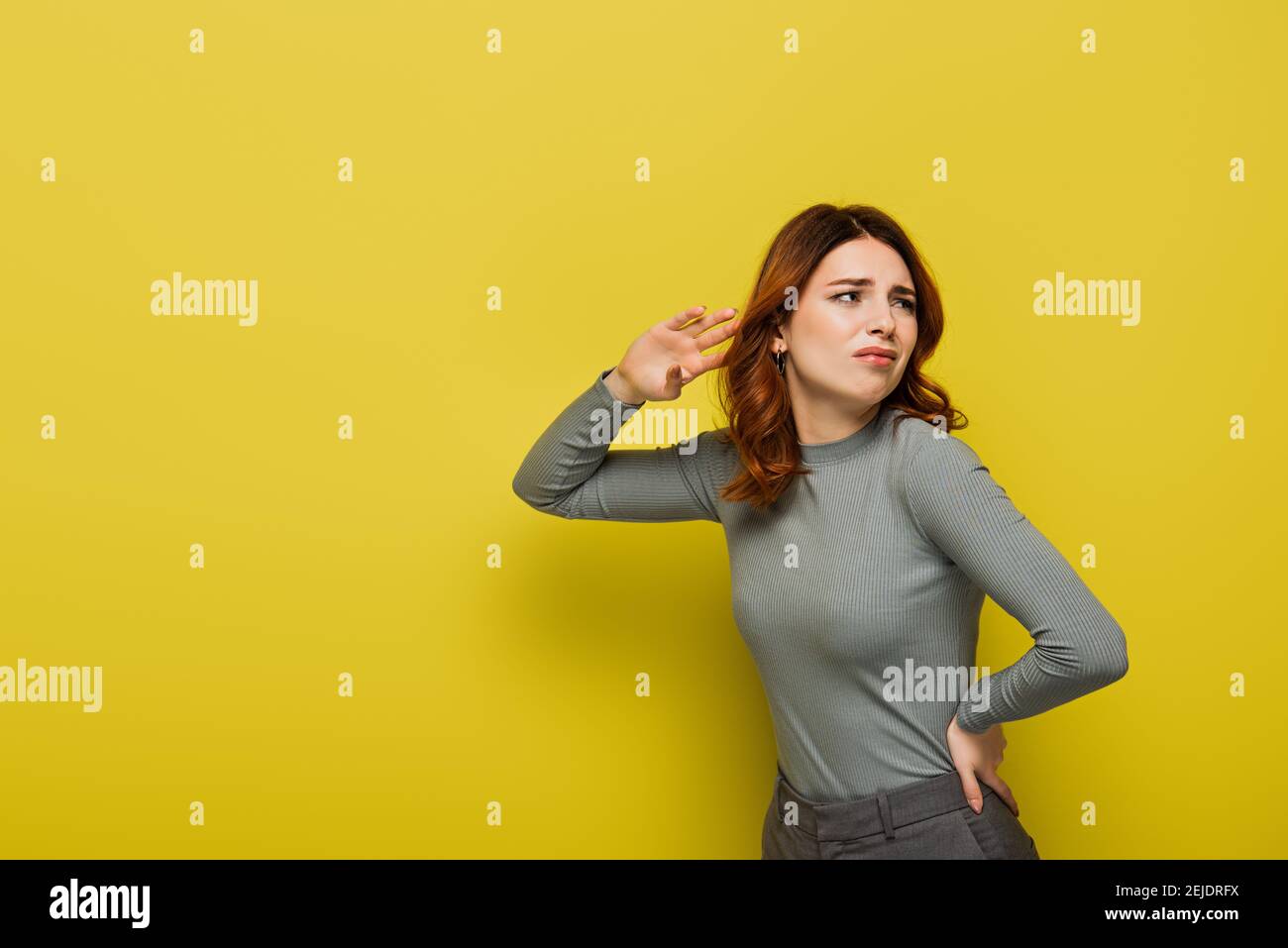 femme mécontentue avec les cheveux bouclés debout avec la main sur la hanche tout en écoutant du jaune Banque D'Images