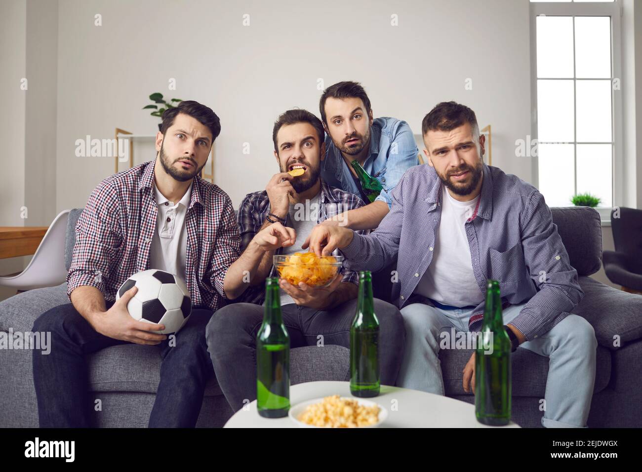 Les hommes regardent un match de football important avec des jetons et de la bière assis à la maison devant la télévision. Banque D'Images