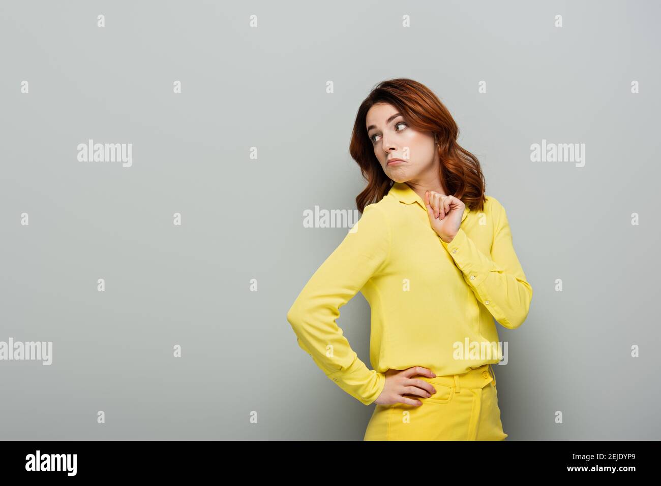 une femme découragée a regardé loin en se tenant debout avec la main sur la hanche en gris Banque D'Images