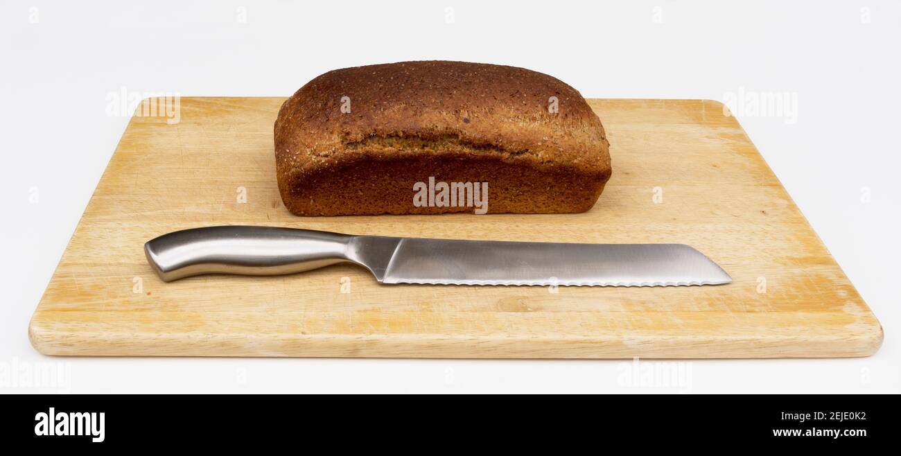 Un pain de pain complet frais et sain est placé sur une planche à découper avec un couteau prêt à être coupé. Banque D'Images