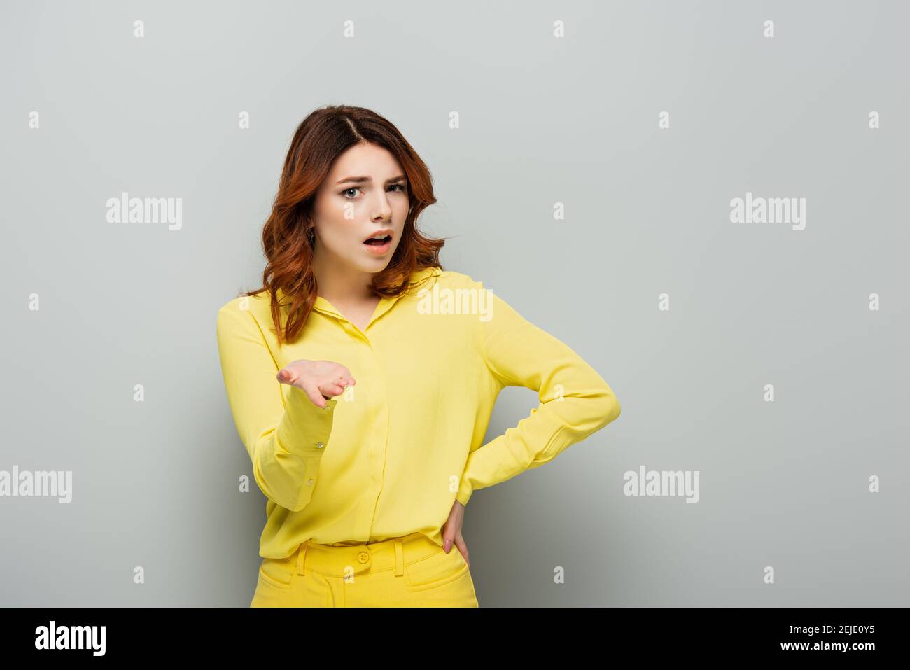 femme choquée pointant avec la main tout en étant debout avec la main sur hanche sur gris Banque D'Images