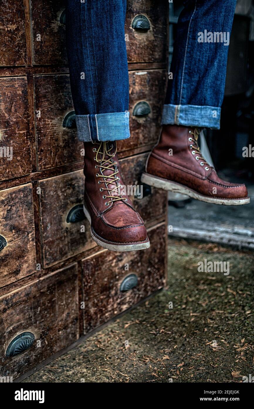 homme portant un jean en denim et des bottes de travail sur un ancien tiroir en bois Banque D'Images