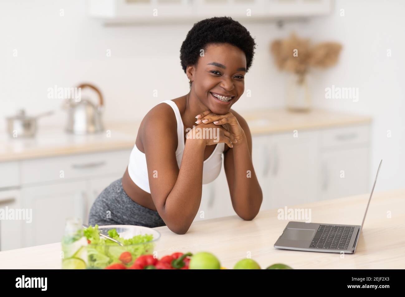 Femme africaine utilisant ordinateur portable Browsing Recettes pour la perte de poids dans la cuisine Banque D'Images