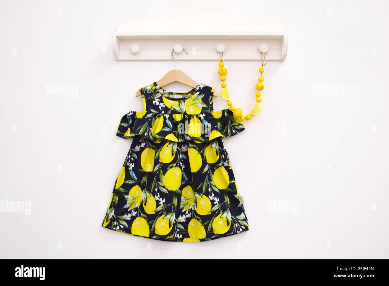Robe de bébé avec motif citron et perles jaunes sur un cintre sur fond clair. Banque D'Images