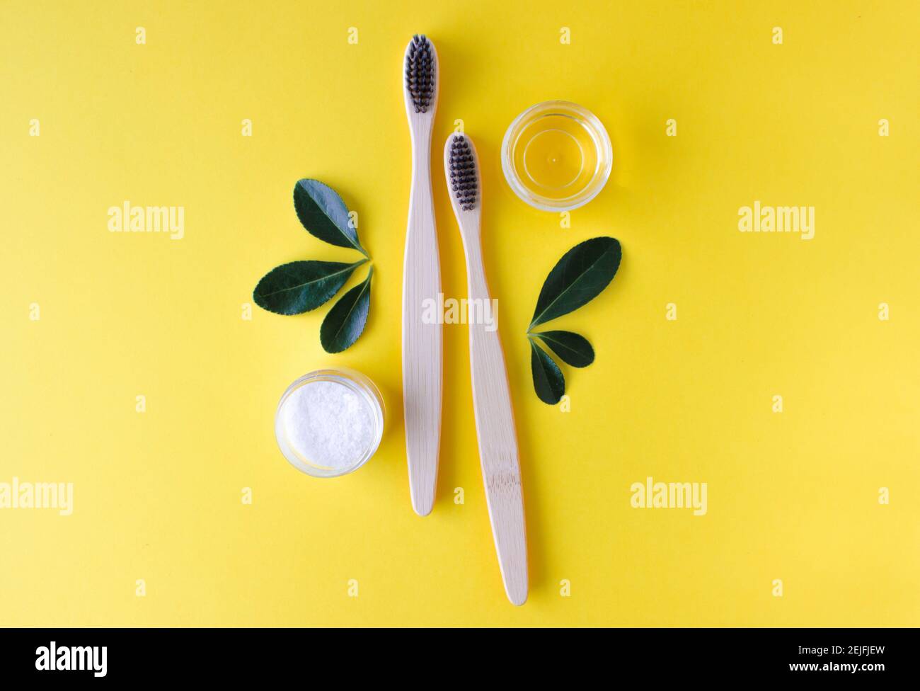 deux brosses à dents écologiques en bambou en bois, dentifrice et feuilles vertes sur fond jaune. Banque D'Images