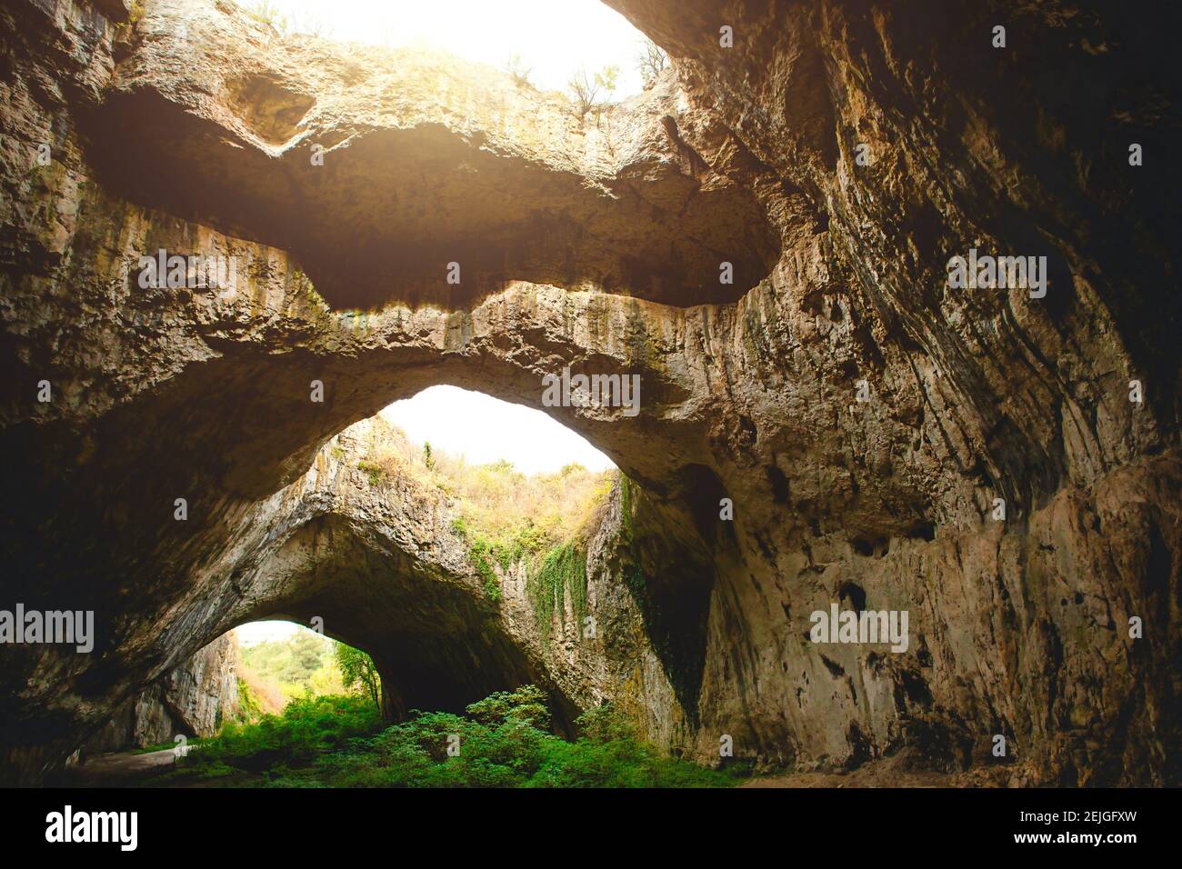 Grotte de Devetashka en Bulgarie - attraction naturelle. De hautes arches d'une immense grotte en pierre avec des trous ronds au sommet, une route touristique avec une clôture à l'intérieur du Banque D'Images