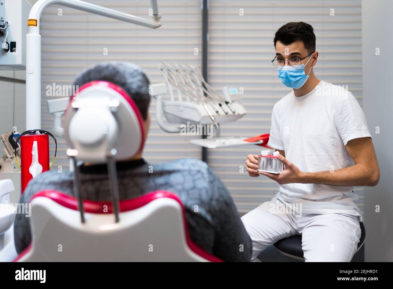 Le chirurgien dentaire avec la couronne dentaire dans les mains modèle parle au patient au sujet des prothèses. Homme au rendez-vous du dentiste Banque D'Images