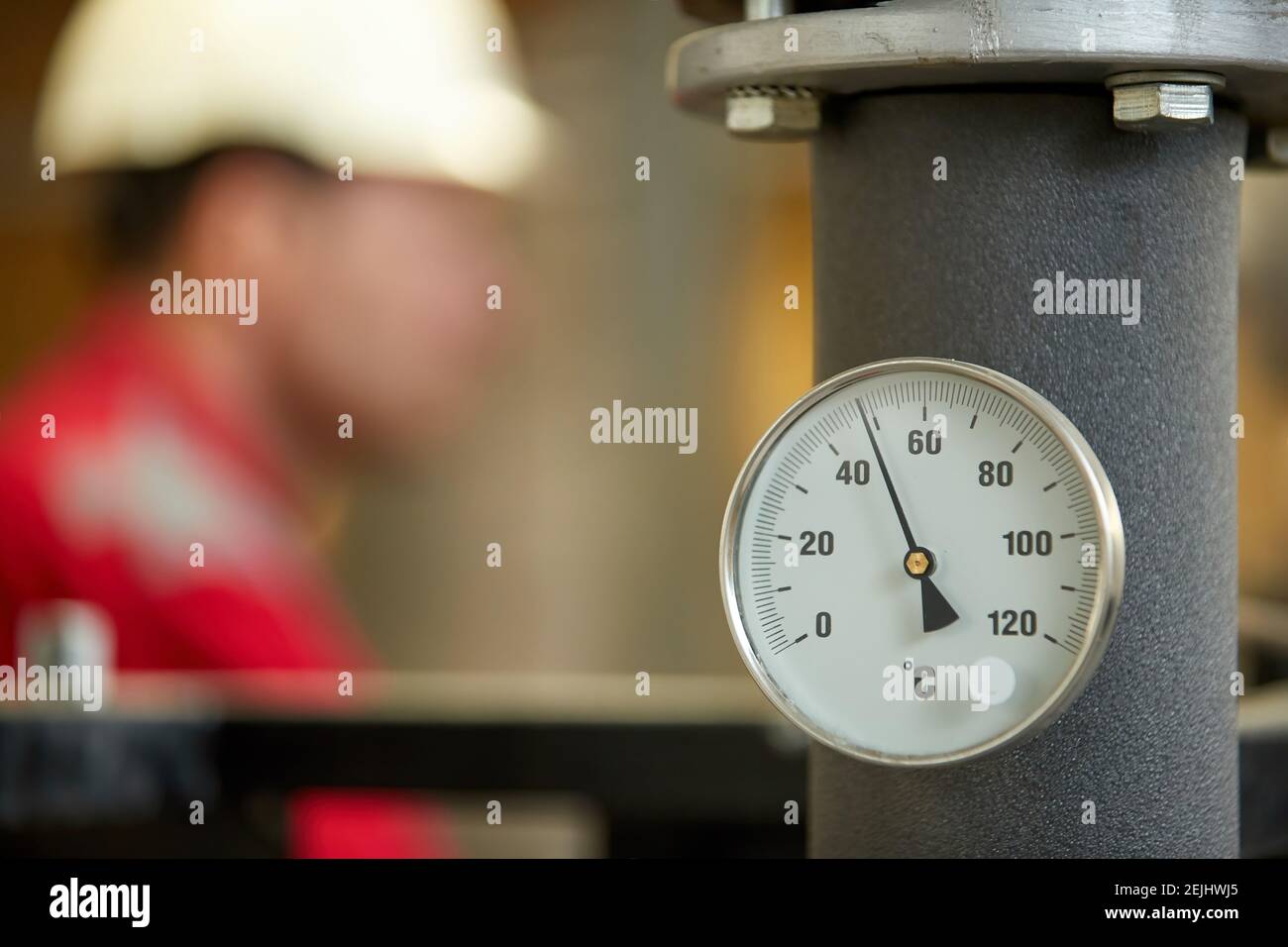 Thermomètre sur le tuyau d'alimentation en eau chaude, système de chauffage. Technicien portant une veste rouge avec un casque blanc paramètres de contrôle. Banque D'Images