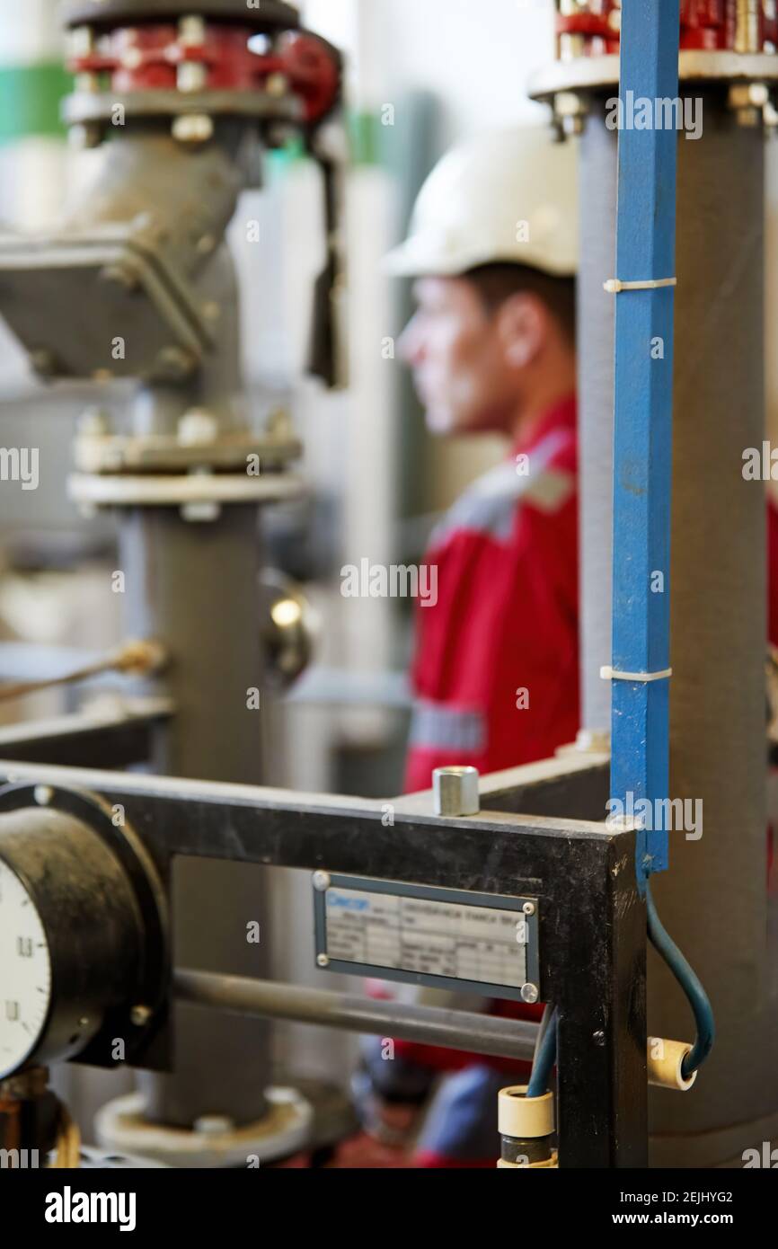 Thème de l'industrie de l'énergie : un technicien en combinaison rouge et casque blanc vérifie les paramètres de chauffage sur les thermomètres. Entretien et inspection. Banque D'Images