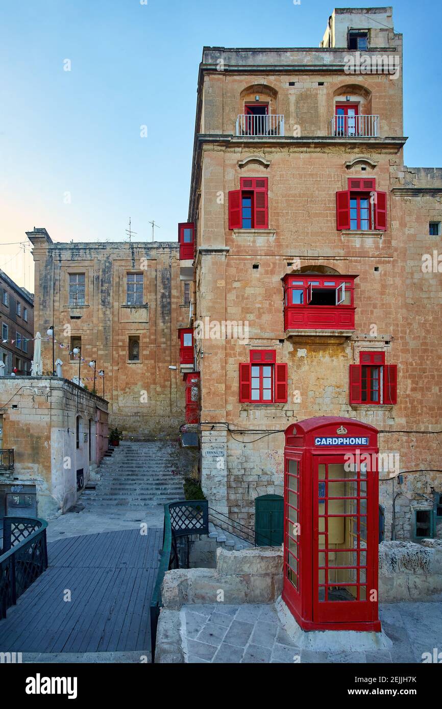 Un kiosque téléphonique rouge profond dans la rue de l'ancienne ville de la Valette dans les couleurs du soir. Verticale, pas de personne. Carte postale. Vacances à Malte. Banque D'Images