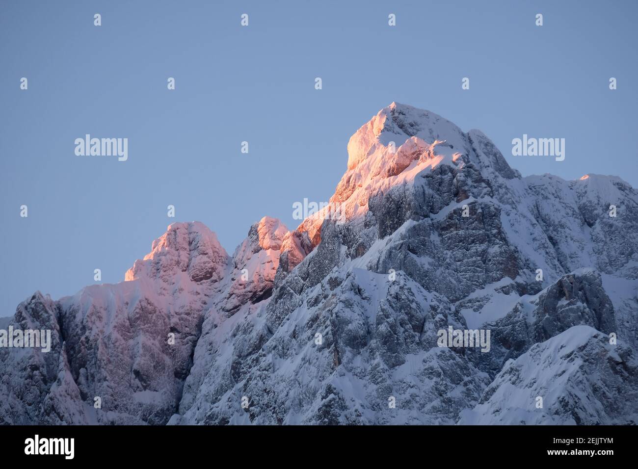 Magnifique gros plan d'un sommet de montagne rose dans les Alpes au coucher du soleil tandis que le vent souffle de la neige au large de la montagne. Puissance des éléments naturels Banque D'Images