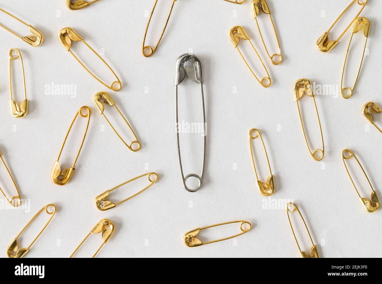 Une grande broche de sécurité argentée entourée de petites broches de sécurité dorées sur fond blanc Banque D'Images