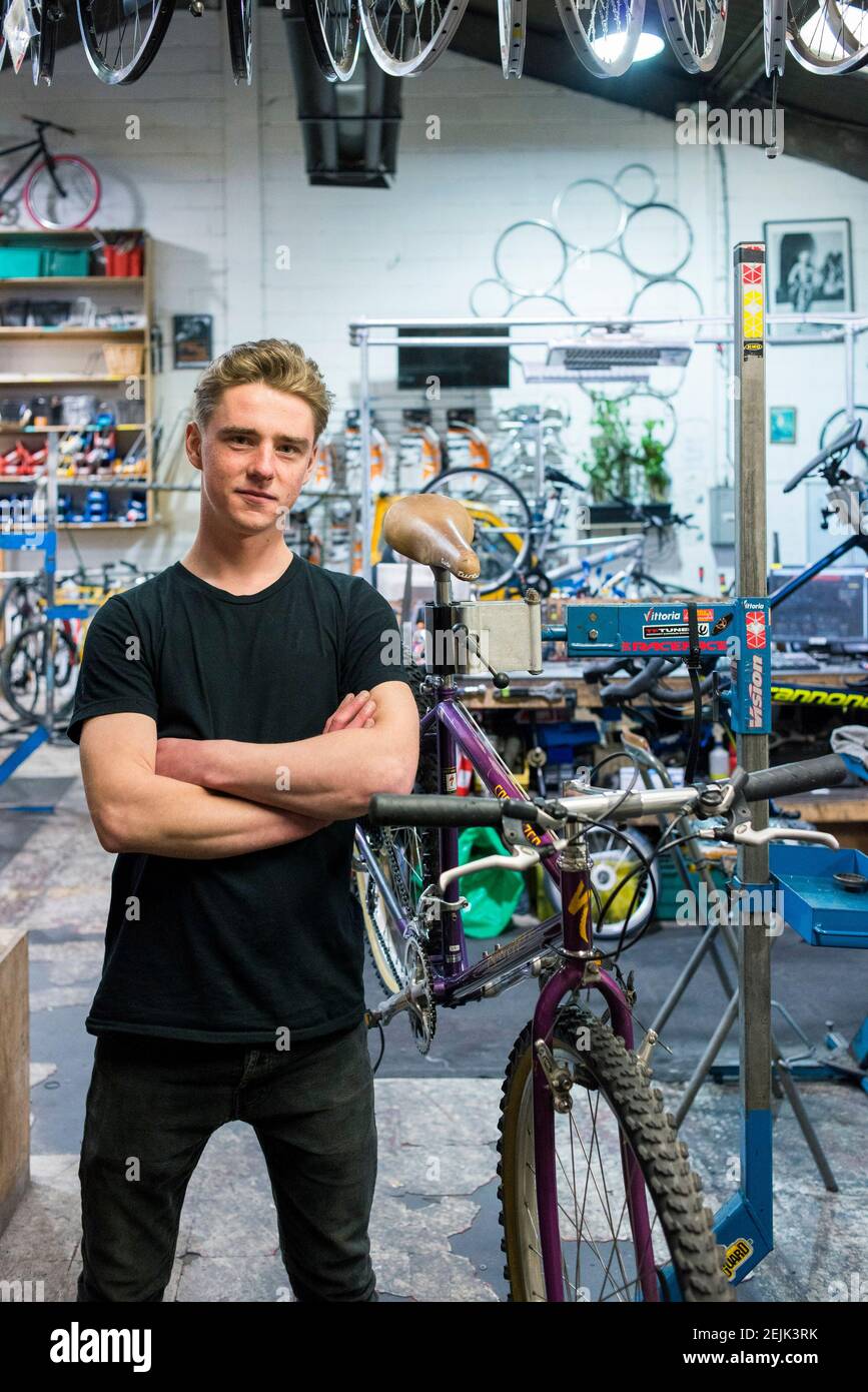 Un technicien de vélo se tient à son poste de travail et pose pour un portrait dans l'atelier d'une entreprise de cyclisme. Banque D'Images