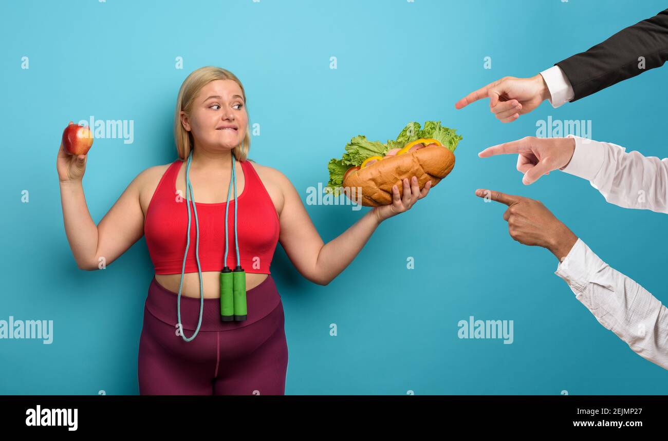 FAT Girl est indécis de manger une pomme ou un grand sandwich. Fond cyan Banque D'Images