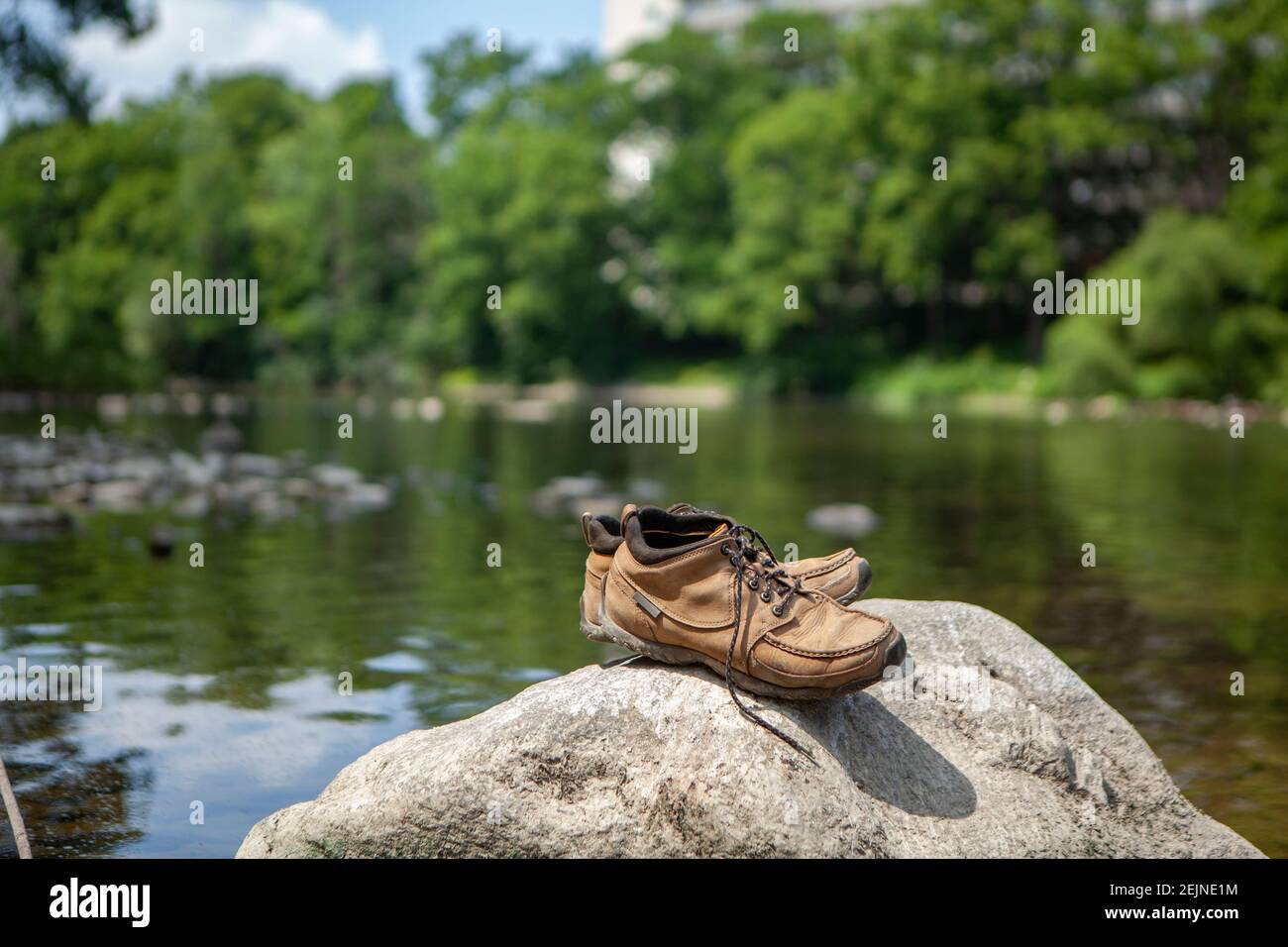 Une paire de chaussures de randonnée brwon debout au bord de la rivière  tandis que personne ne repose leurs pieds douloureux et les trempette dans  l'eau fraîche de la rivière pour se