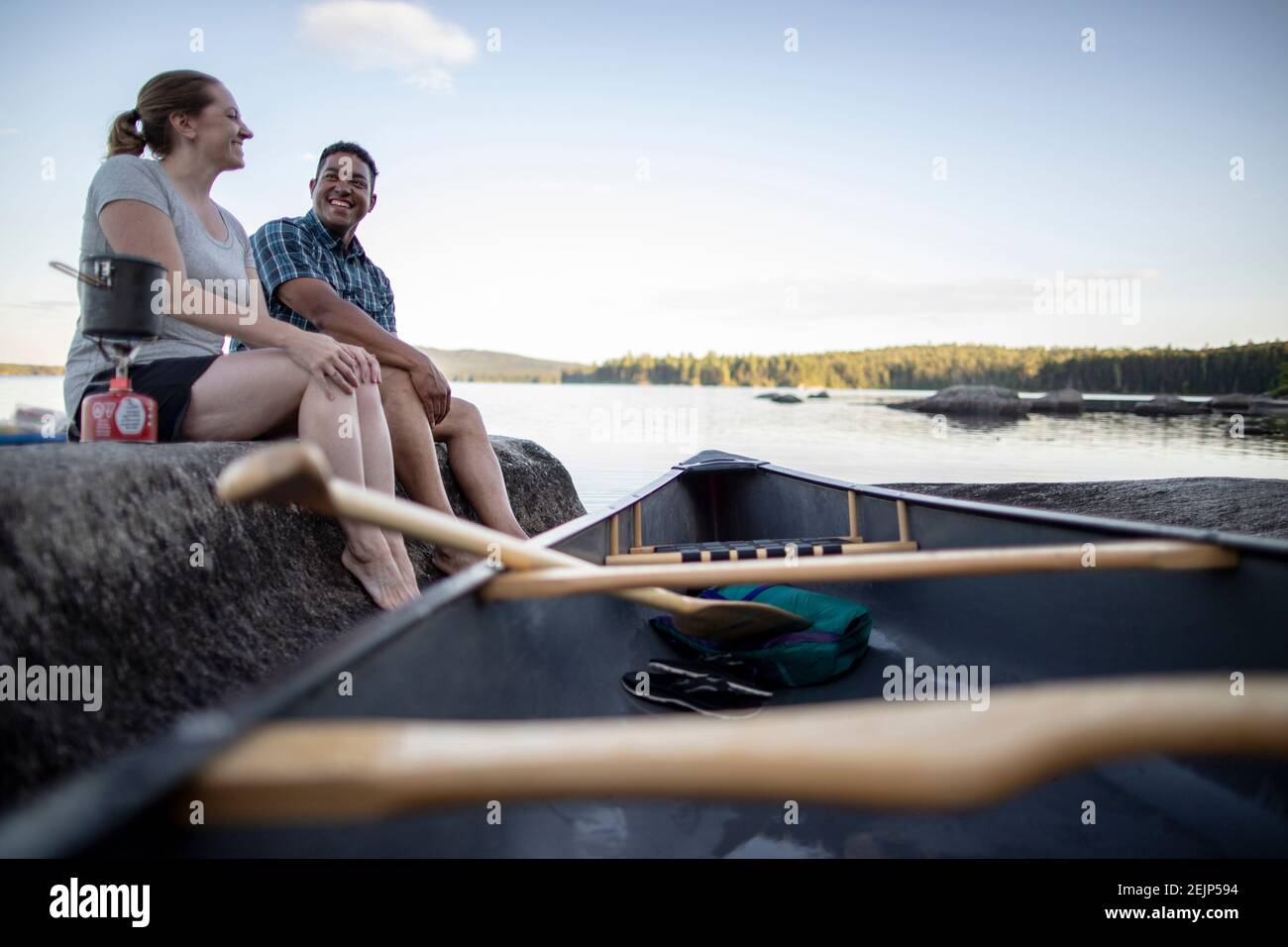 L'homme afro-américain et la femme blanche s'assoient sur le rocher lac avec canoë Banque D'Images