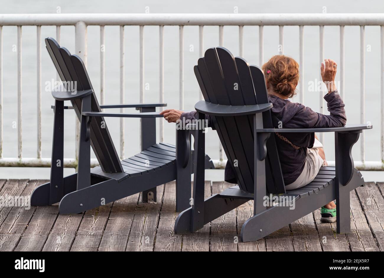 Femme solitaire adulte assise sur une chaise en bois sur la jetée regardant la chaise vide à côté d'elle. Tristesse et tristesse. Vue sur la rue, mise au point sélective. Banque D'Images