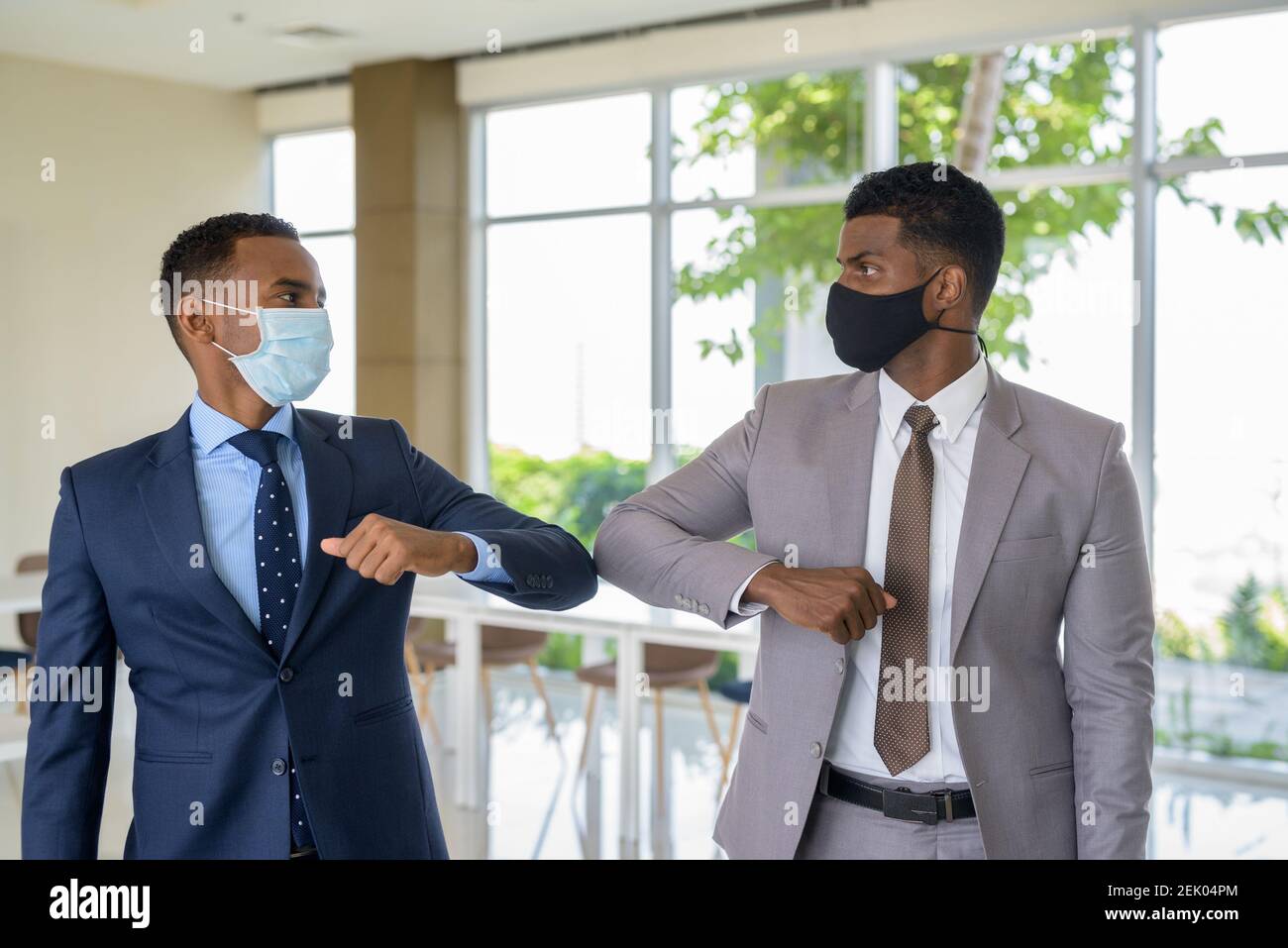 Deux hommes d'affaires africains portant un masque médical tout en saluant avec une bosse de coude saluant au bureau. Concept de distance sociale pendant le coronavirus Banque D'Images