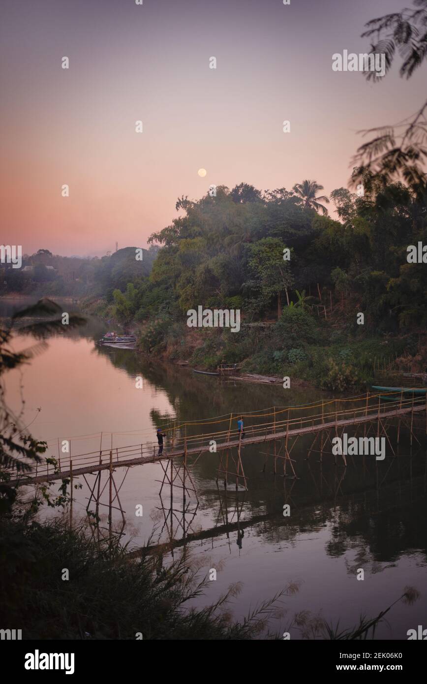 Coucher de soleil le long de la rivière Nam Khan au pont de bambou À Luang Prabang avec la pleine lune dans le ciel Banque D'Images