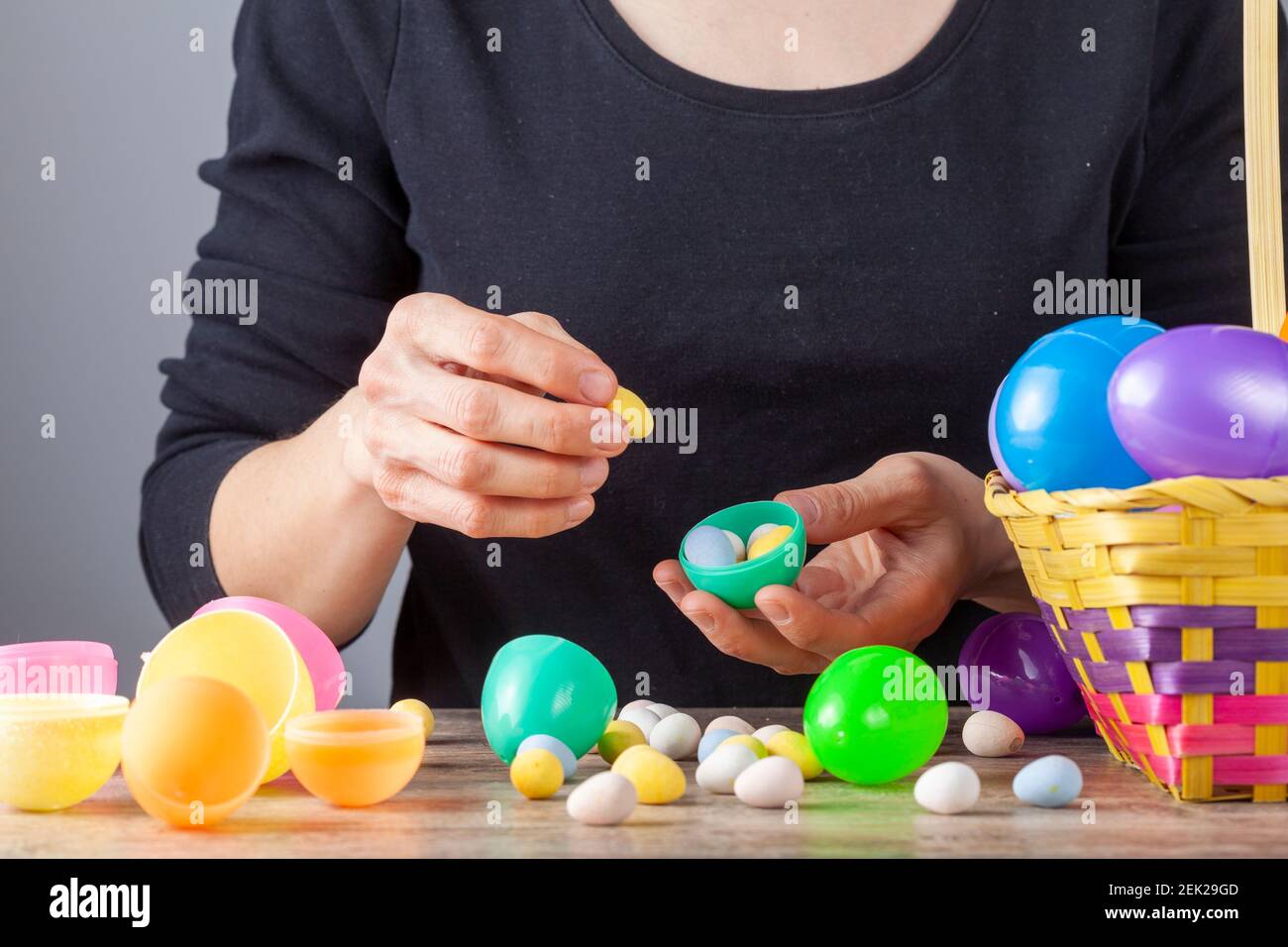 Une femme caucasienne remplit des coquilles d'oeufs de pâques en plastique avec des oeufs de chocolat enrobés de sucre croquant en préparation pour la célébration de pâques. Elle met le Banque D'Images