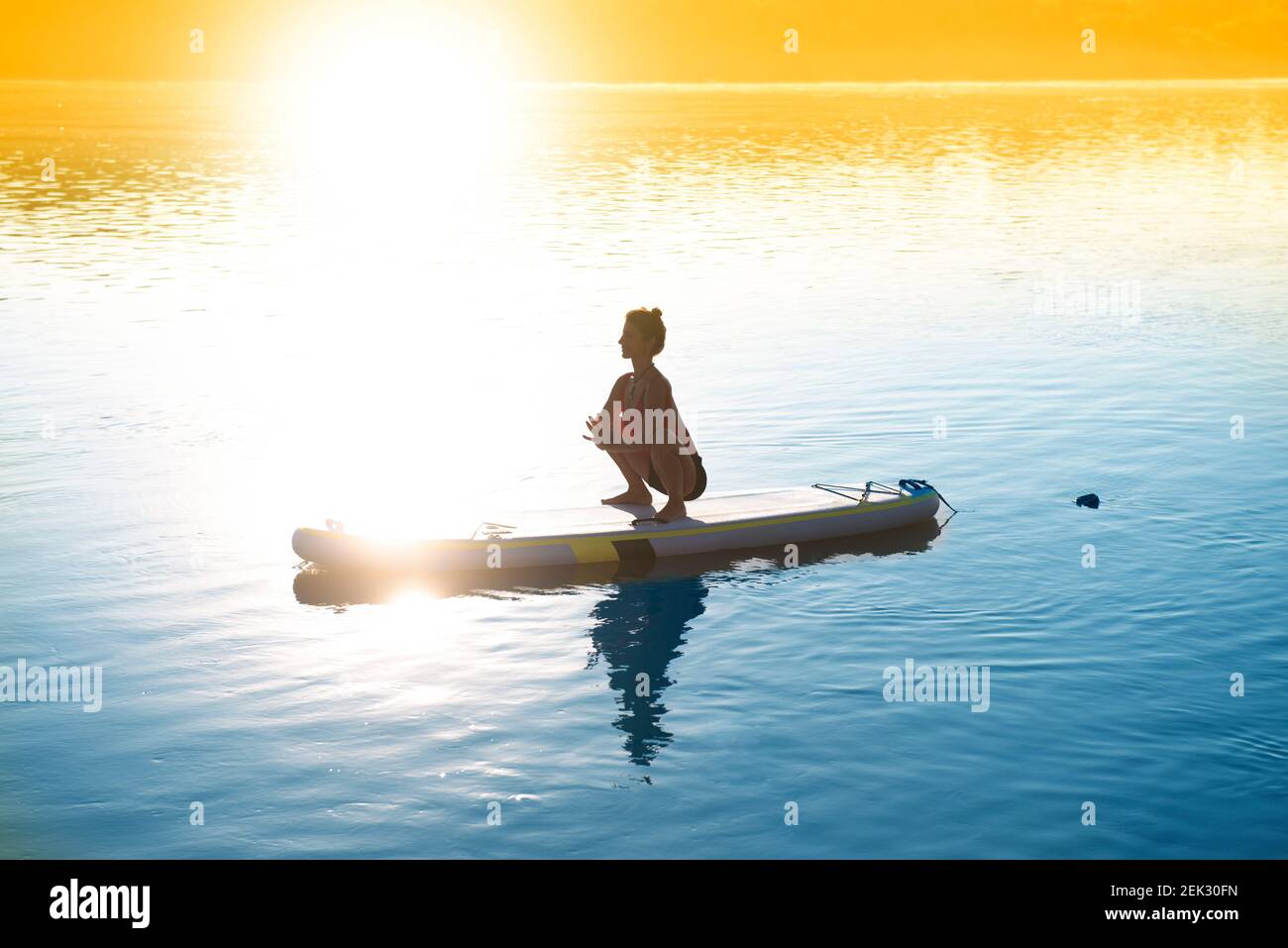 Femme méditant et pratiquant le yoga au lever du soleil sur un paddleboard Banque D'Images