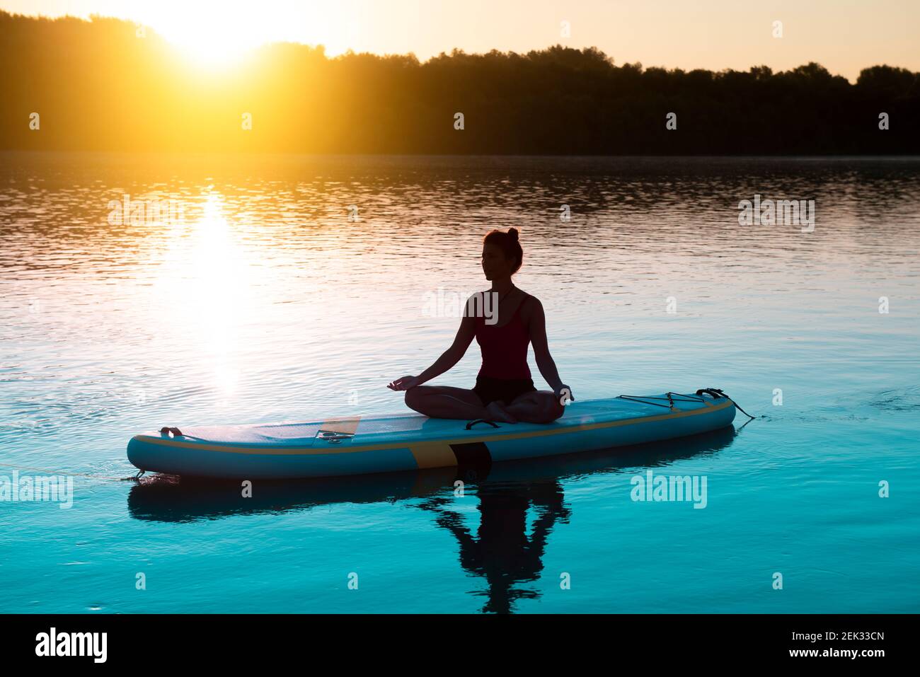 Femme méditant et pratiquant le yoga au lever du soleil sur un paddleboard Banque D'Images