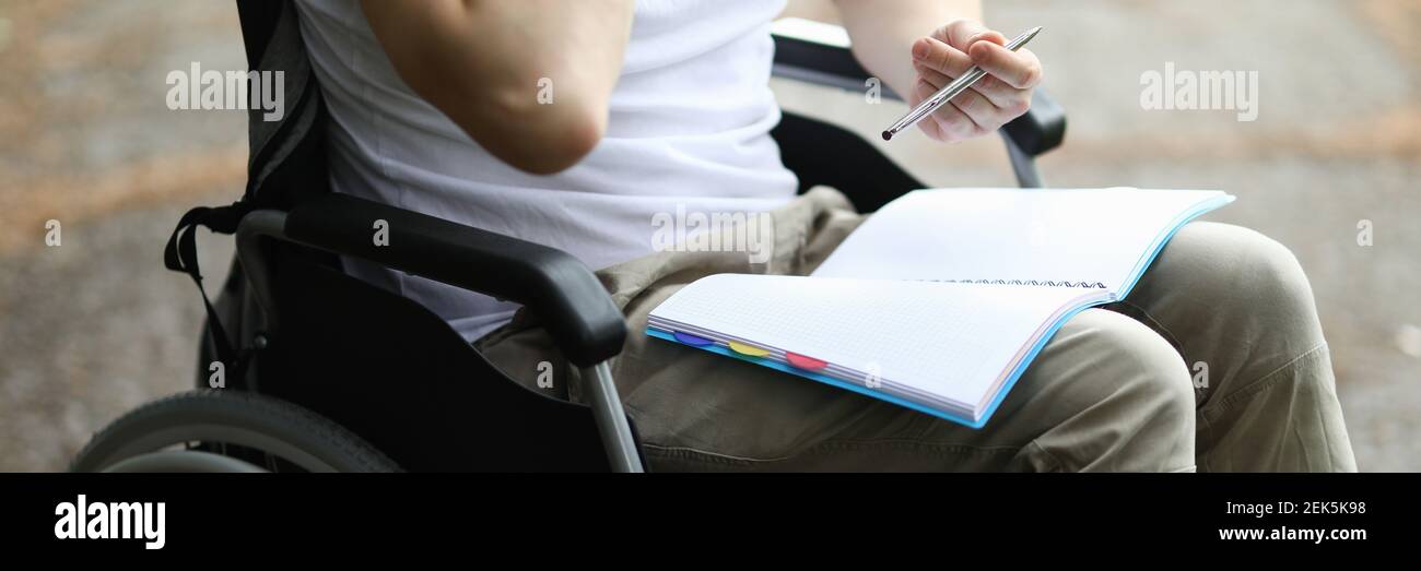 Homme assis en fauteuil roulant et prendre note dans le carnet dans le parc. Banque D'Images