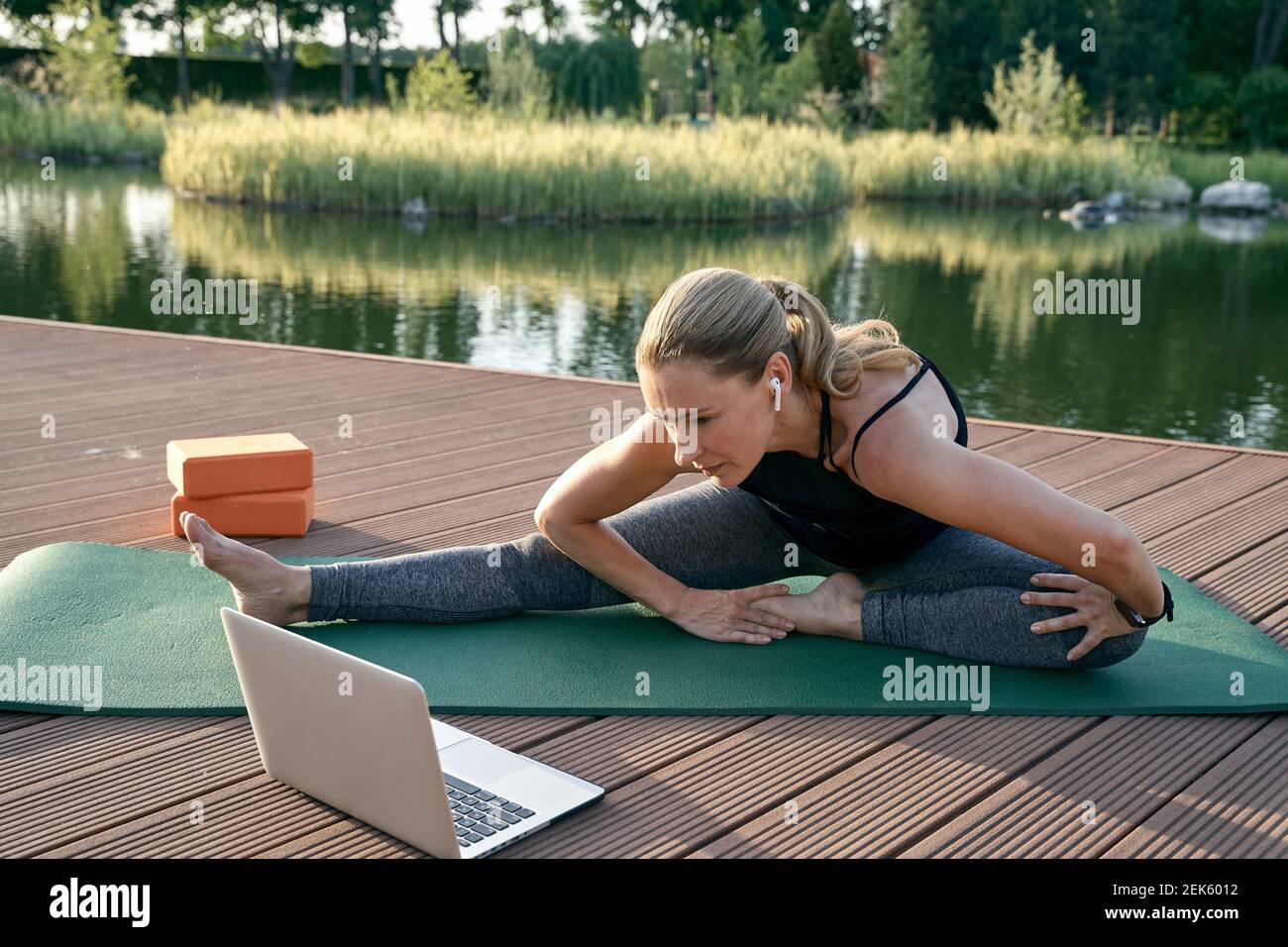 Découvrez le yoga. Sportive attrayante femme d'âge moyen regardant un tutoriel sur un ordinateur portable tout en faisant du yoga sur un tapis dans la nature, par une journée ensoleillée Banque D'Images