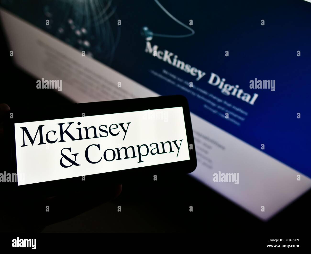 Personne tenant un téléphone portable avec le logo de la société de conseil en gestion McKinsey Company à l'écran en face de la page Web d'affaires. Mise au point sur l'affichage du téléphone. Banque D'Images