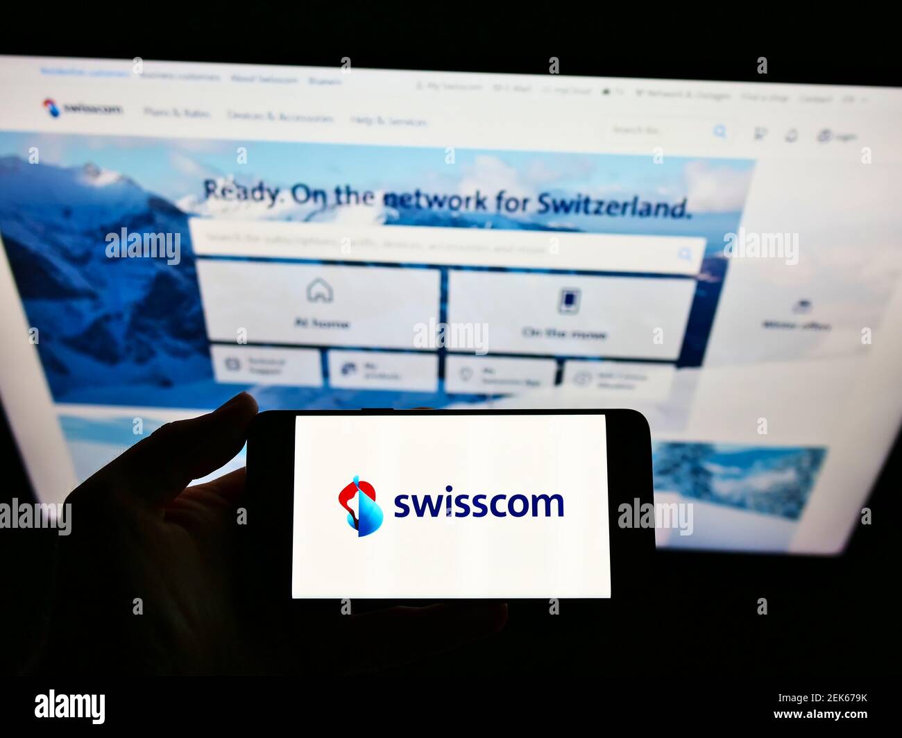Personne tenant un smartphone avec le logo de la société suisse de télécommunications Swisscom AG à l'écran devant le site. Mise au point sur l'affichage du téléphone. Banque D'Images