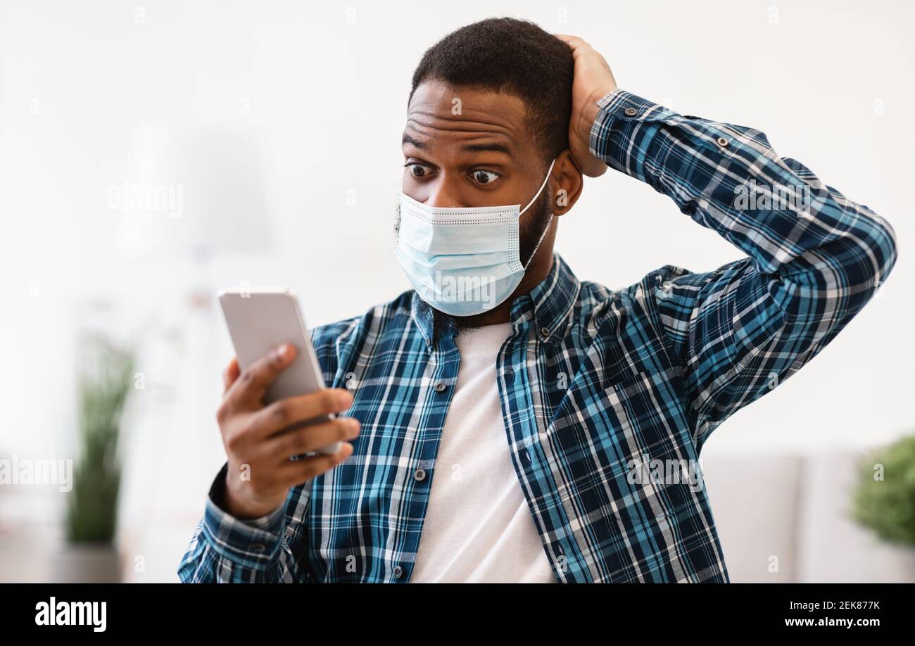 Un homme choqué utilise un téléphone portant un masque facial assis sur son lieu de travail Banque D'Images