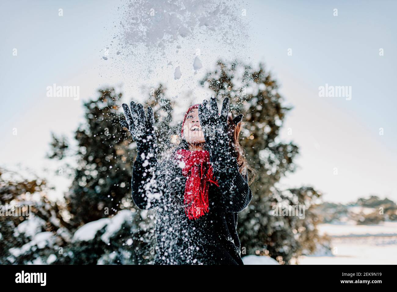 Une femme espiègle qui jette de la neige tout en profitant de l'hiver à la campagne contre ciel dégagé Banque D'Images
