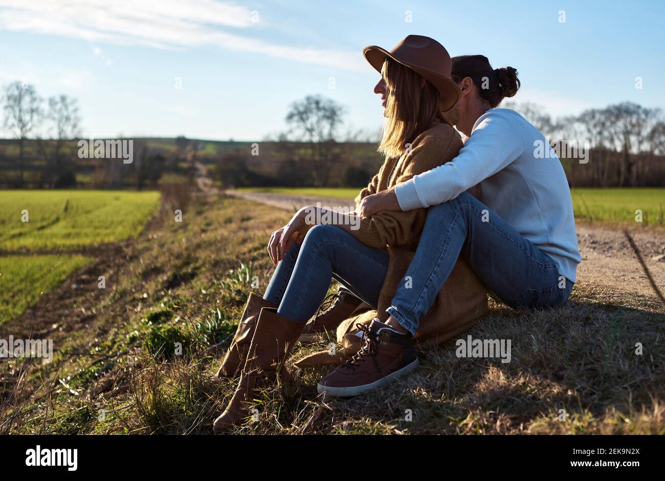 Couple hétérosexuel assis sur le terrain pendant le coucher du soleil Banque D'Images