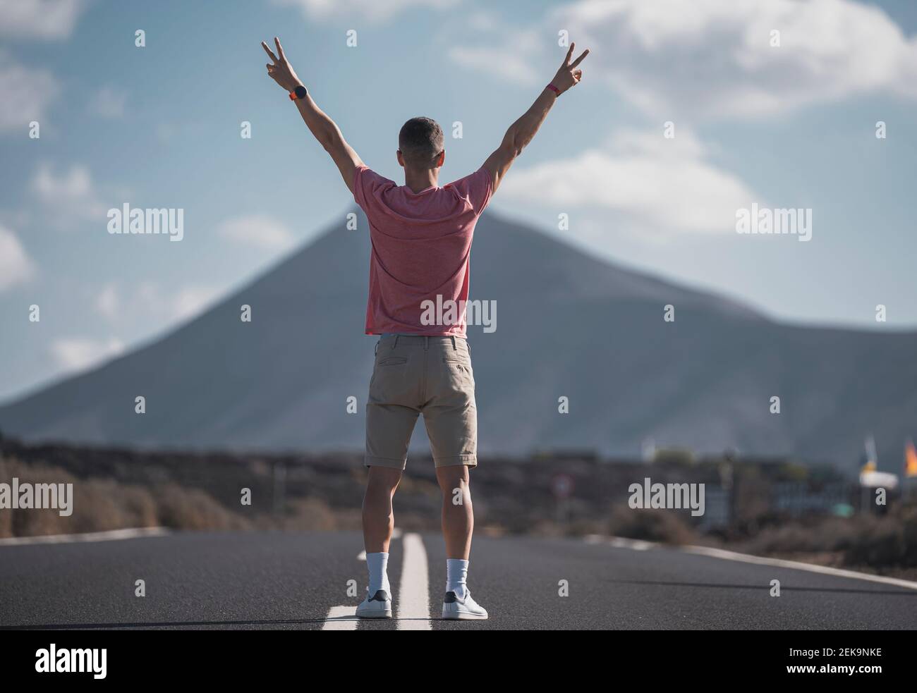 Jeune touriste mâle faisant un geste de paix en face de la roche volcanique à Lanzarote pendant les vacances, Espagne Banque D'Images