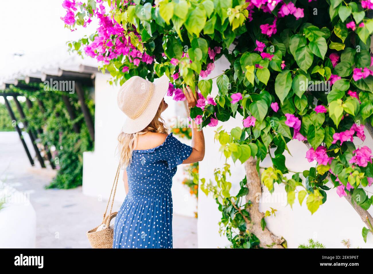 Femme mature portant un chapeau qui sent des fleurs qui poussent à l'usine au village de Binibeca, Minorque, Espagne Banque D'Images