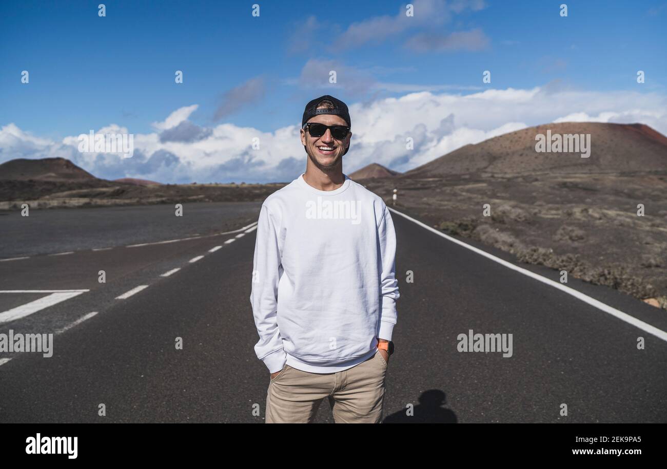 Souriant touriste mâle avec les mains dans les poches contre le volcan El cuervo à Lanzorte, Espagne Banque D'Images