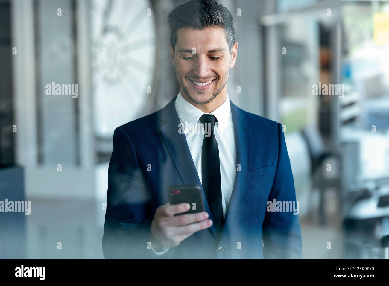 Un entrepreneur souriant portant un costume à l'aide d'un téléphone portable lorsqu'il est debout bureau Banque D'Images