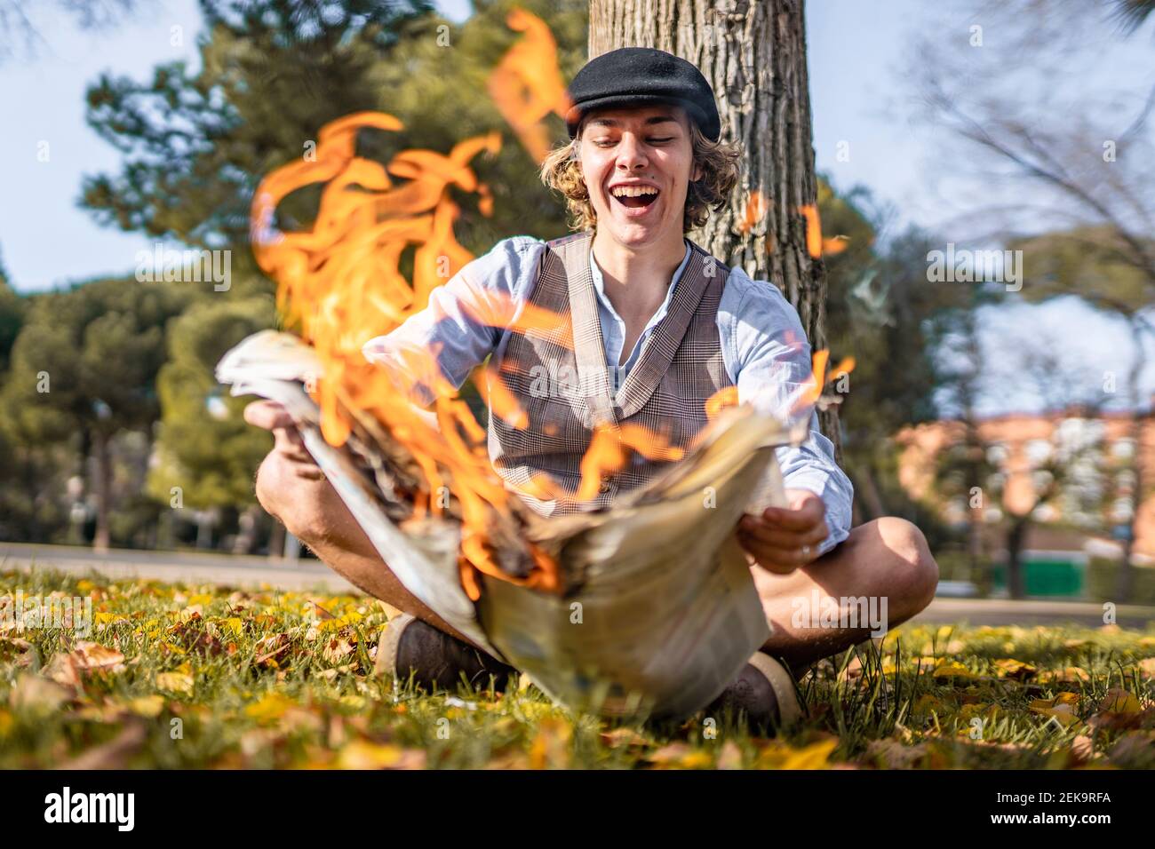 Un jeune homme joyeux lisant un journal éclairé tout en se sittng dans le parc Banque D'Images
