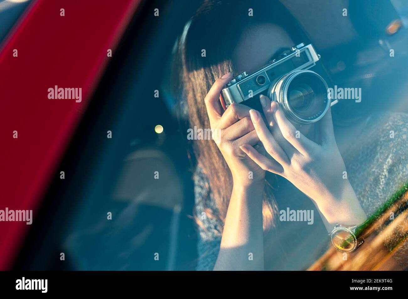 Jeune femme photographiant depuis un appareil photo d'époque à travers une fenêtre en verre de voiture Banque D'Images