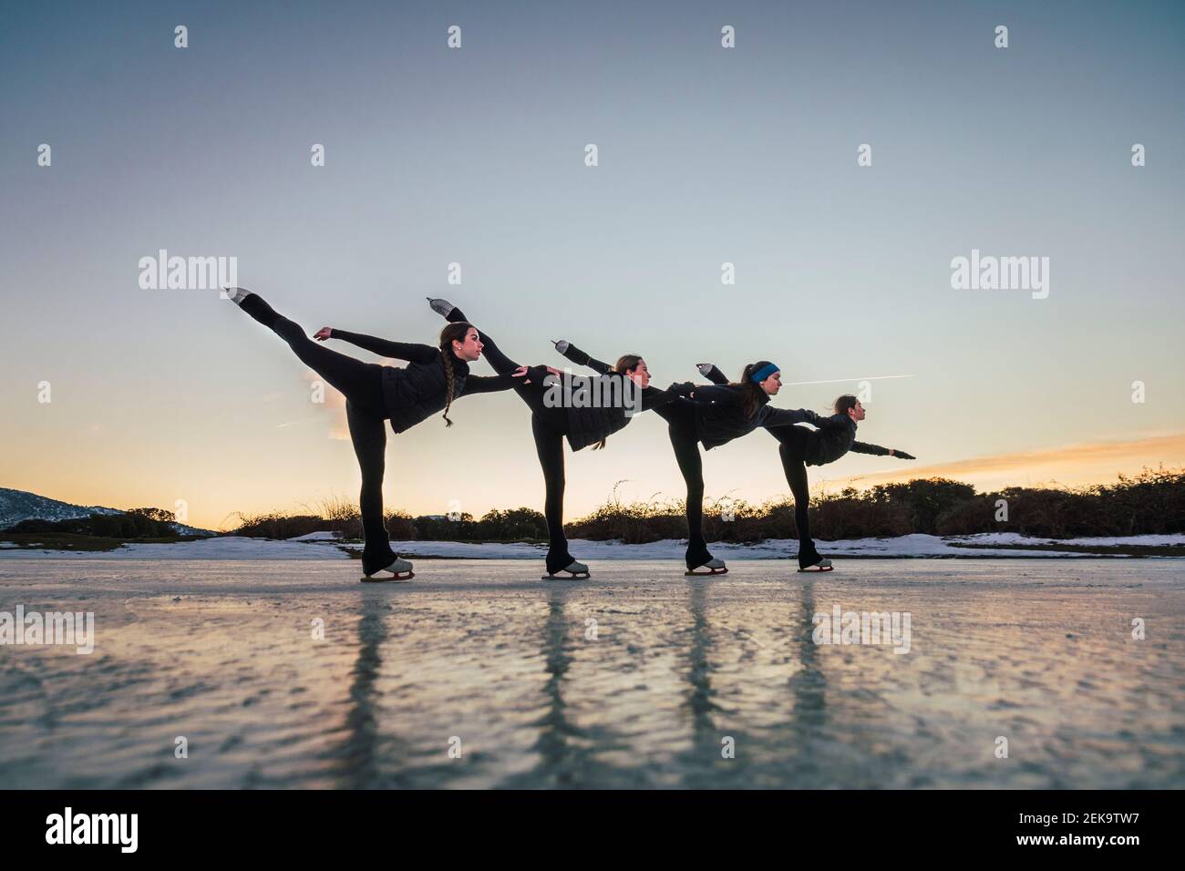 Patineurs féminins pratiquant sur un lac gelé au crépuscule Banque D'Images